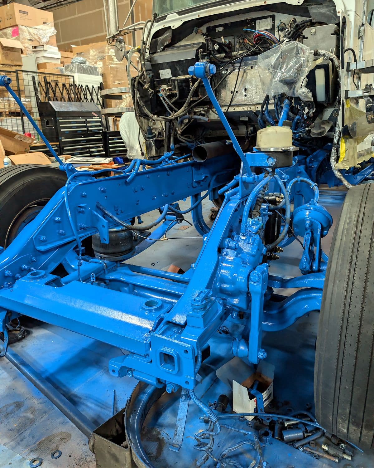 Painted blue front frame rails and suspension of a semi truck during a custom air ride installation